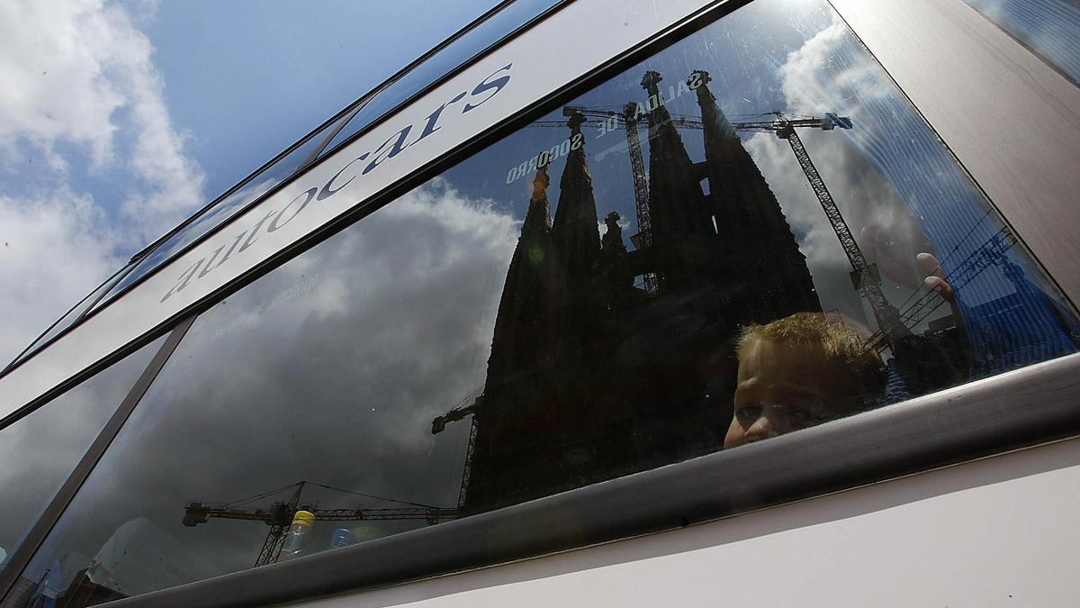 Un autocar turístico, con la Saghrada Família reflejada en el cristal.