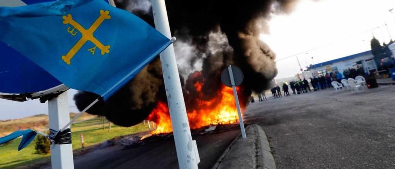 Una bandera de Asturias ondea a la entrada de la fábrica de aluminio de San Balandrán; en segundo término, una barricada en llamas y, al fondo, trabajadores concentrados en una pasada movilización.