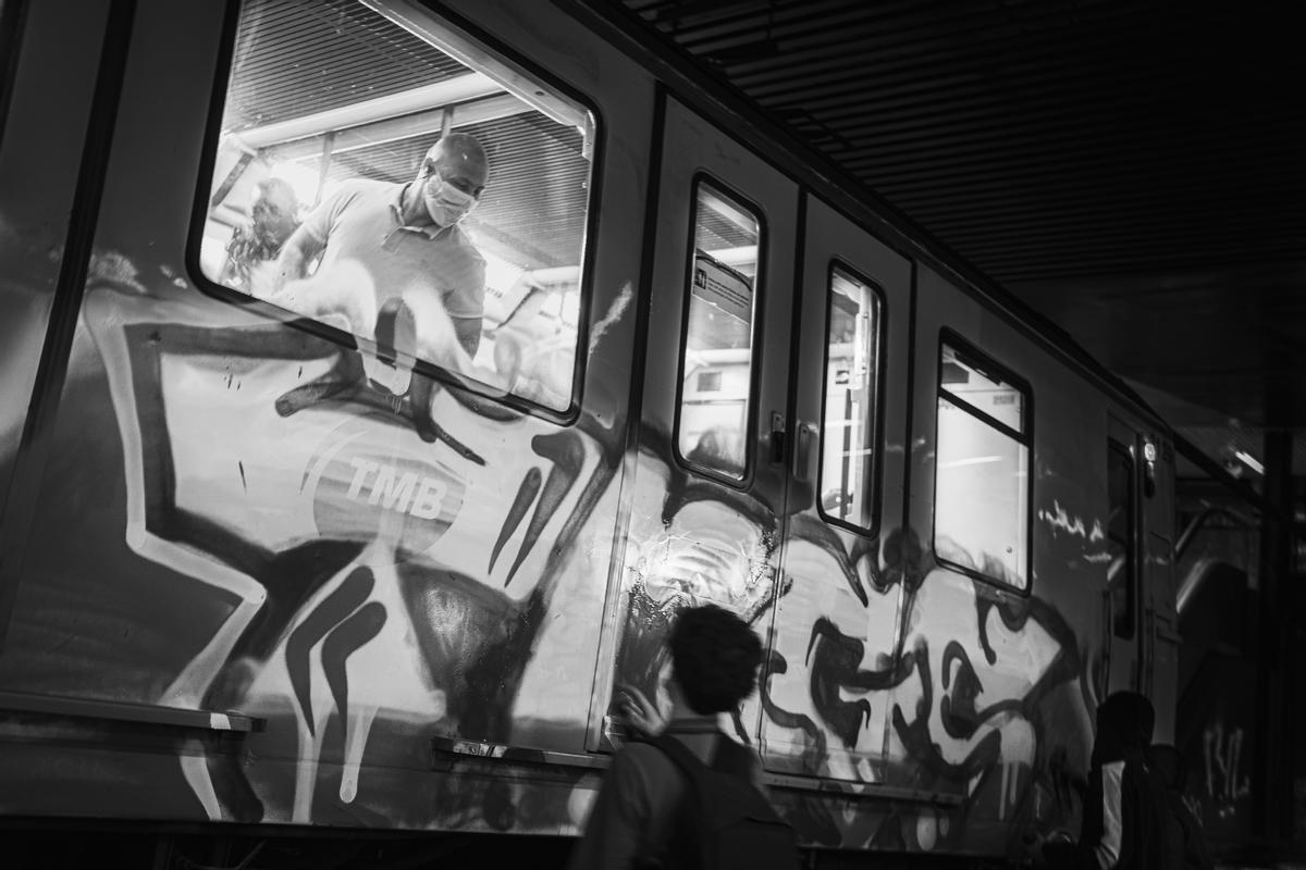 Un pasajero del metro de Barcelona observa a través de la ventana como los escritores pintan el vagón de tren en el que viajaba. Estos han accionado la palanca de frenado de emergencia, y entre tres han pintado en tres minutos el vagón del metro.