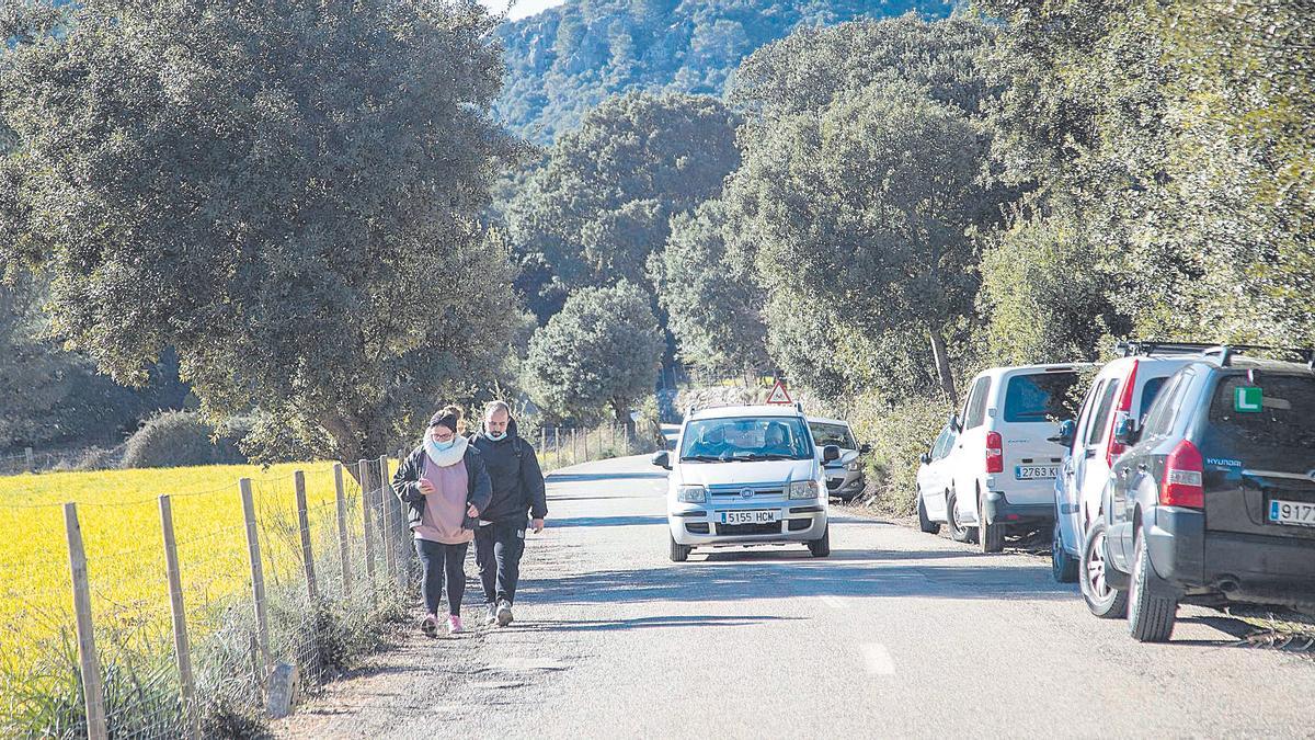 Dos senderistas caminan el pasado domingo hacia el inicio de la ruta. A la derecha, cola de coches aparcados.