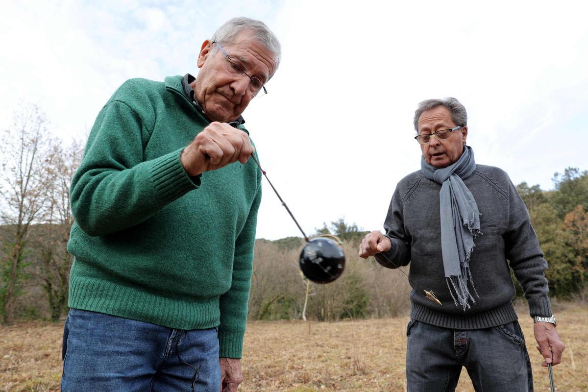 Los zahoríes españoles Enric Colom y Lluis Sarsanedes Bosch (R) muestran cómo buscan agua con péndulos y varillas en un campo en Sant Feliu de Pallerols, cerca de Girona, el 15 de enero de 2024. Cataluña lucha contra una sequía histórica durante tres años, y algunos residentes ya experimentando restricciones de agua en su vida diaria.