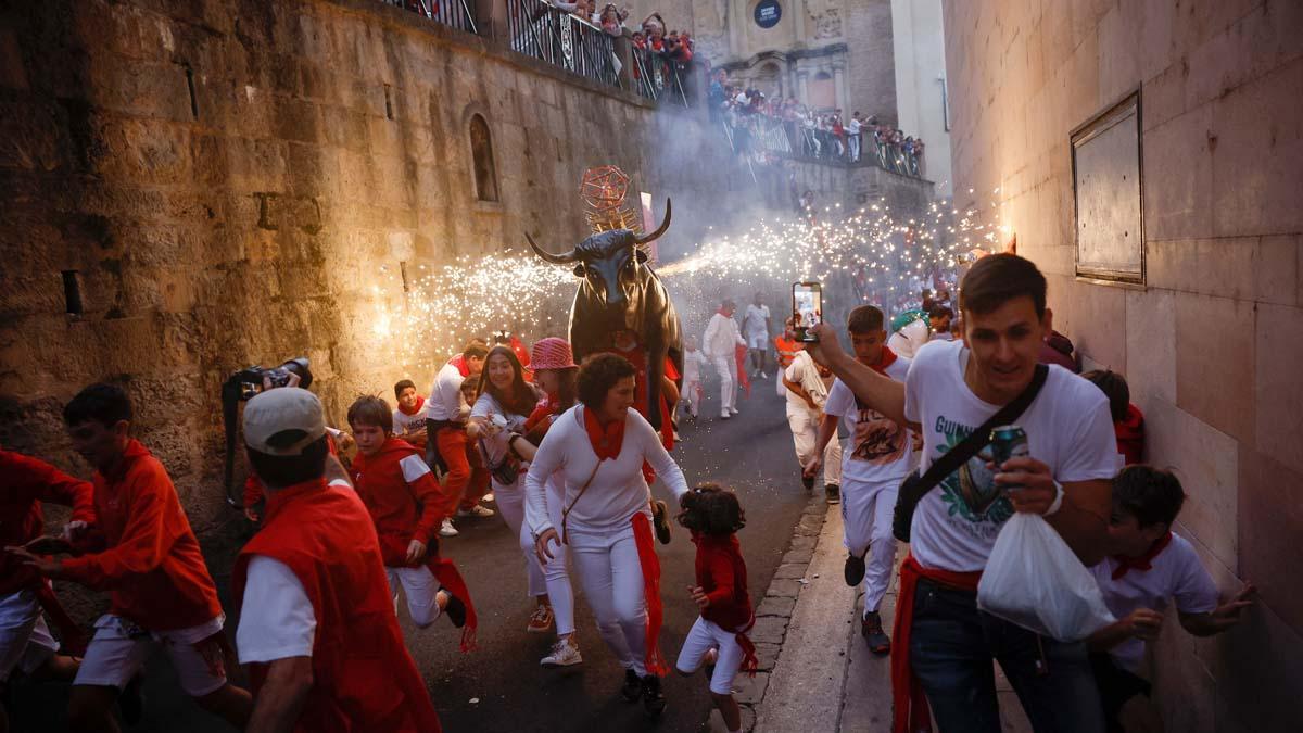 Los juerguistas corren junto al Toro de Fuego, un hombre que lleva una figura de toro llena de fuegos artificiales, durante el festival de San Fermín en Pamplona.