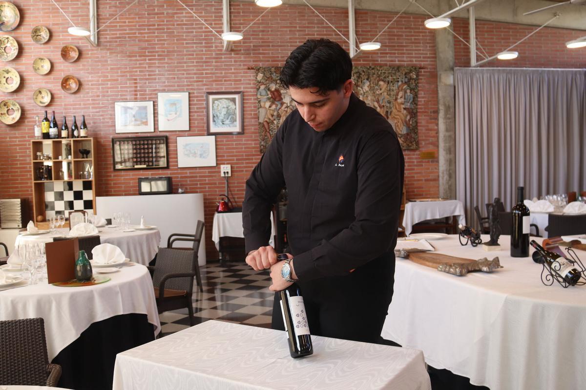 Un alumne de l'Escola d'Hostaleria i Turisme de Girona obre una ampolla de vi per fer pràctiques de sommelier