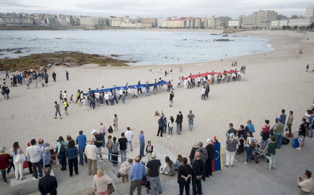 La comunidad venezolana despliega en la playa de Riazor una bandera para exigir que su país sea "libre".