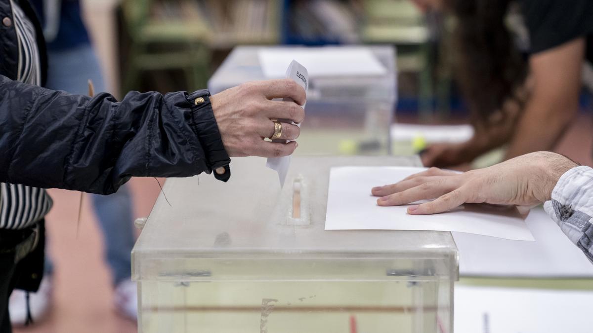 Una persona mete su voto en la urna en un colegio electoral.