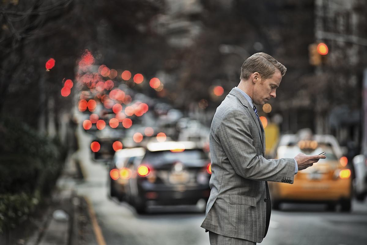 Un hombre revisando su teléfono antes de cruzar la calle