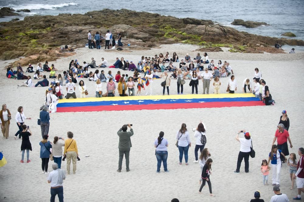 La comunidad venezolana despliega en la playa de Riazor una bandera para exigir que su país sea "libre".