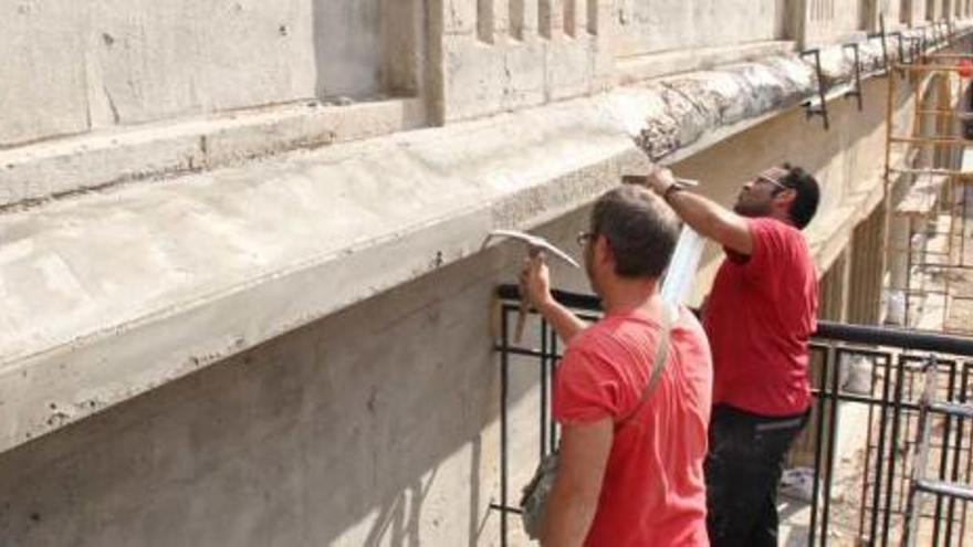 Dos operarios trabajando en el saneamiento de la pasarela de hormigón, que presenta tanto grietas como desconchados.