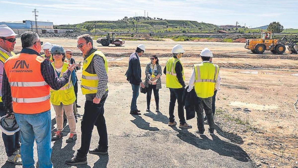 Personal de las empresas que participan en la obra y del ayuntamiento, en la parcela, con dos máquinas al fondo.