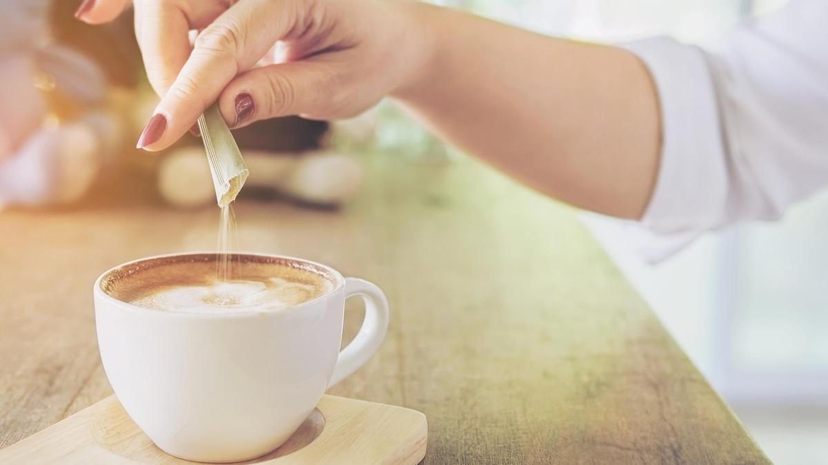 Una mujer añade azúcar en una taza de café con leche.
