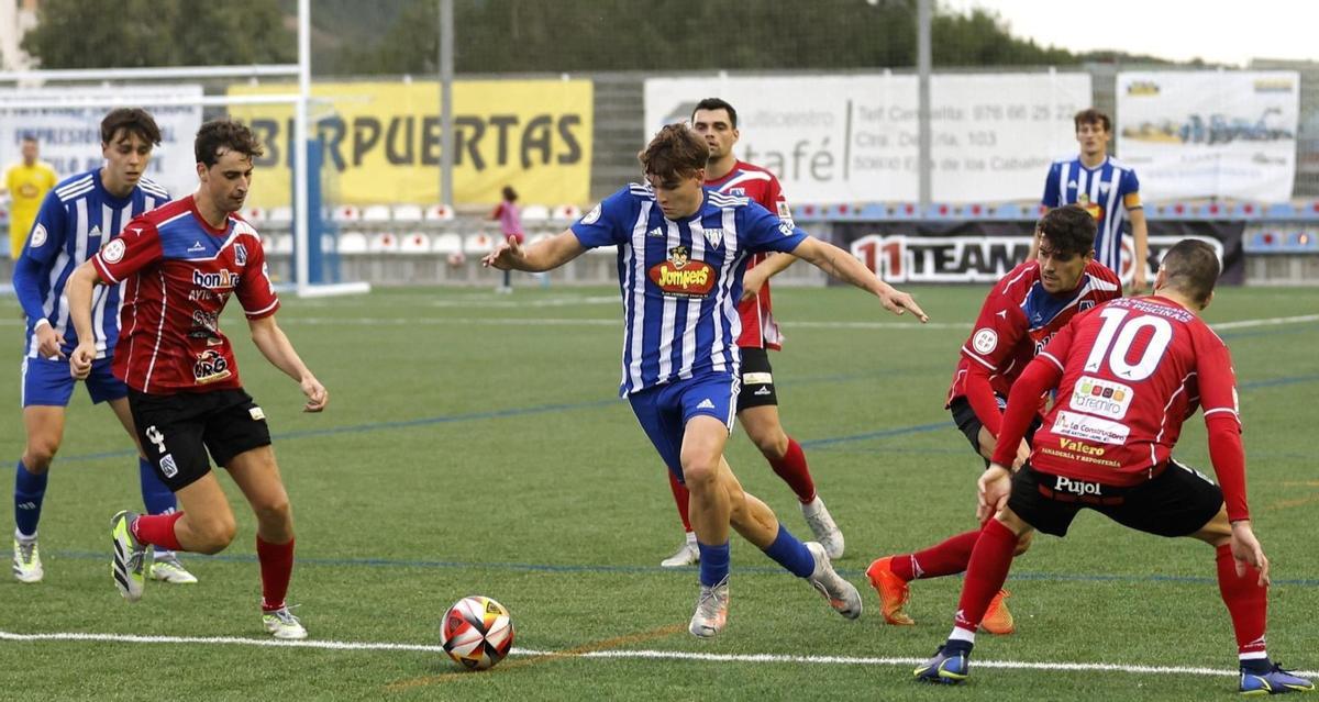 Un futbolista de la SD Ejea trata de avanzar con el balón en presencia de varios jugadores rivales en un encuentro de su equipo.