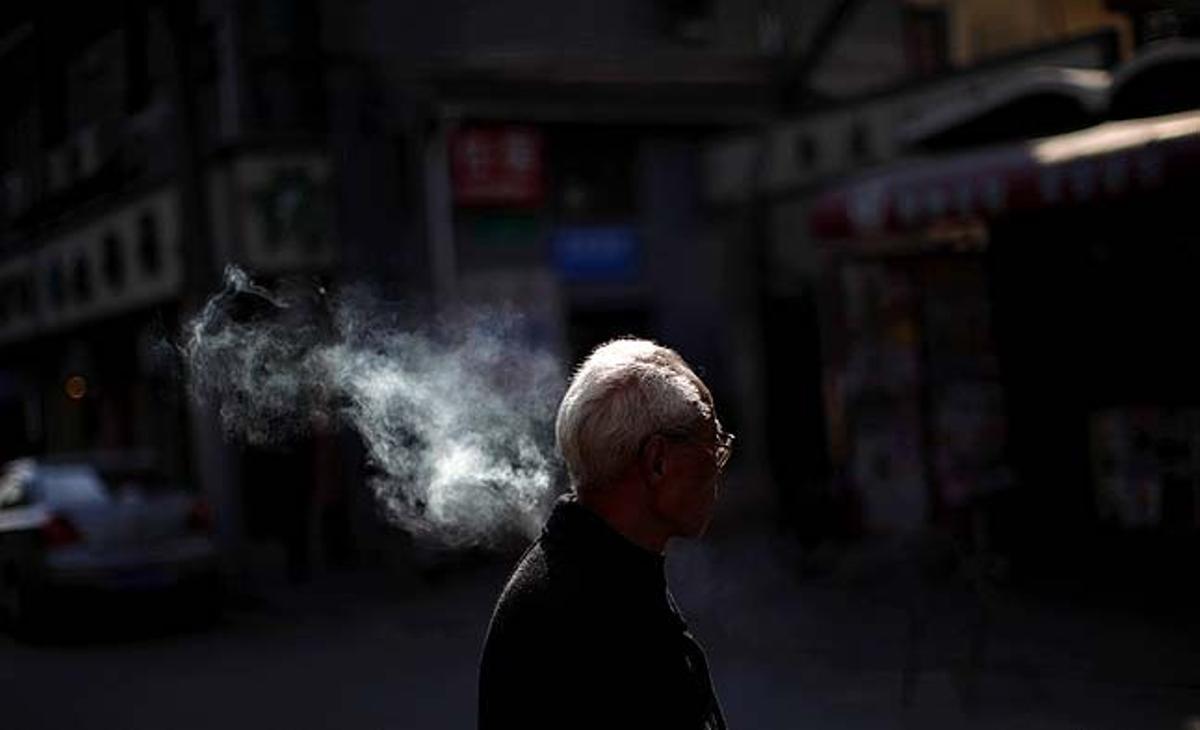 Un home fa una pausa mentre es fuma un cigarret a la cantonada d’un carrer al centre de Xangai (Xina).