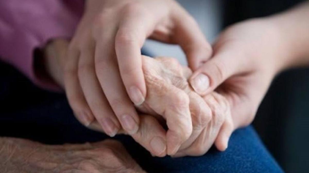 Una cuidadora toma la mano de una mujer con Parkinson.