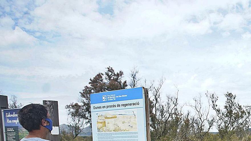 Un home observant un cartell que anuncia la regeneració de les dunes de la zona de la Gola del Ter, a l’Estartit