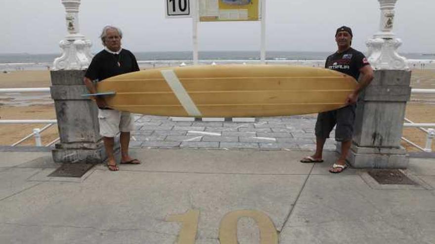 Luis Fueyo y Pepe More sujetan la primera tabla de surf que se utilizó en Gijón, que pesa 17 kilos y mide 3,30 metros, frente a la escalera 10 del muro de San Lorenzo. | ángel gonzález