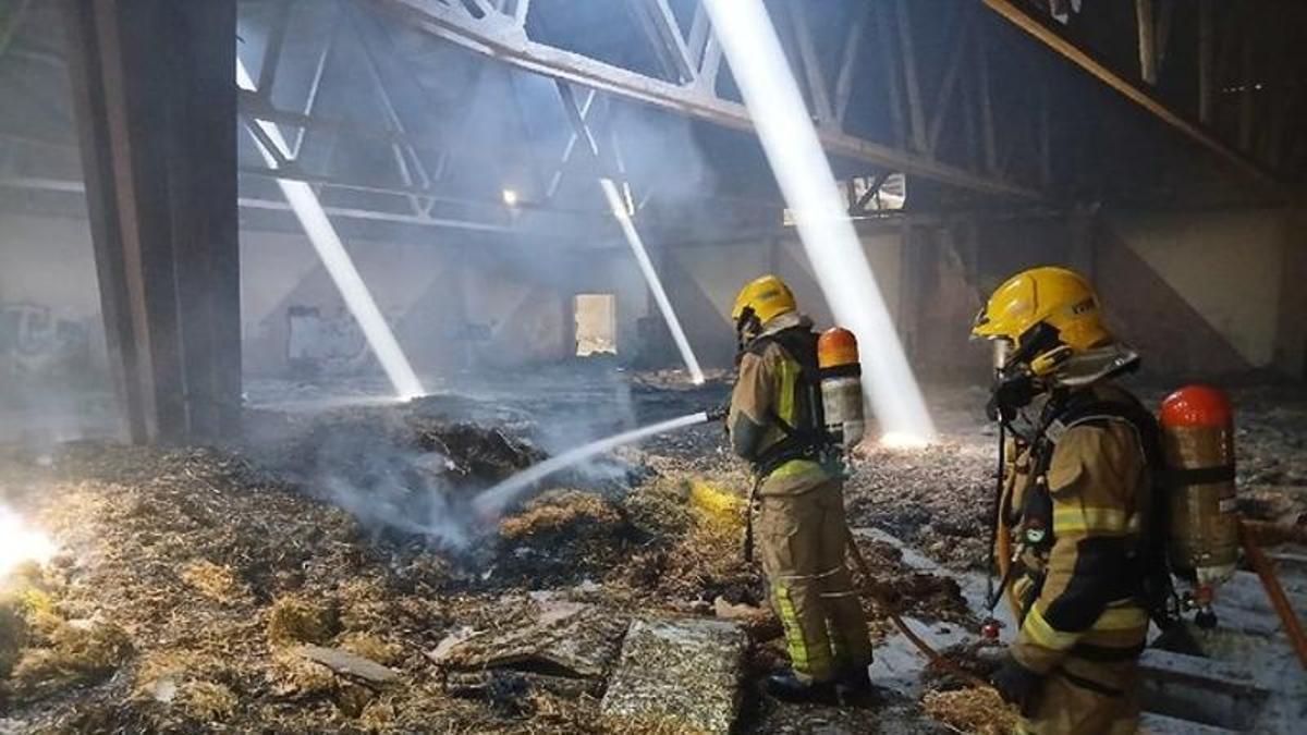 Els bombers apagant l'incendi a l'interior de la nau on ha cremat la palla