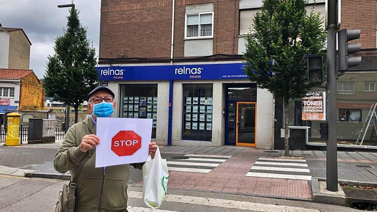 Anselmo Díaz, ayer, con su cartel de “Stop” y la bolsa en la que lleva el chaleco, frente a uno de los semáforos apagados en la avenida de Oviedo, en Lugones. | I. G.