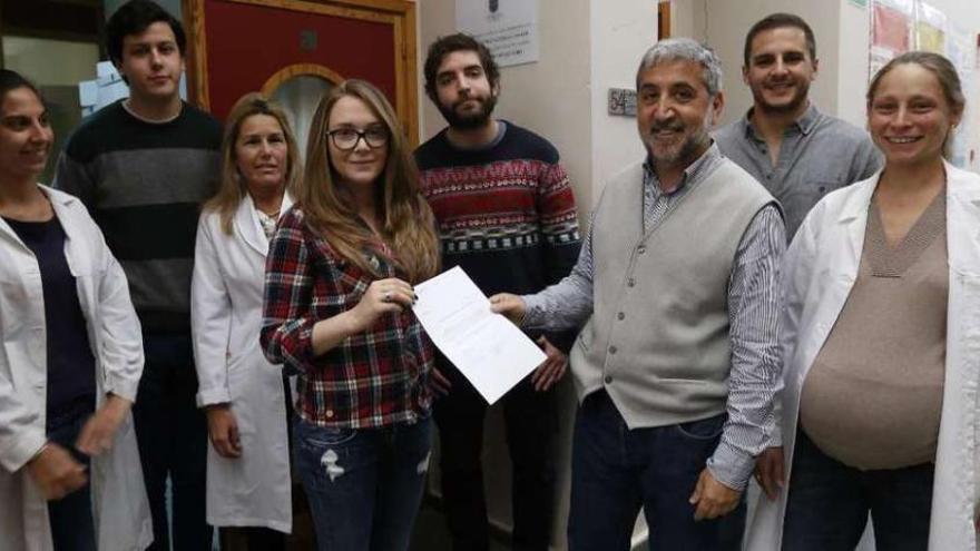 Soliño hace entrega dela recaudación a Berrocal a la entrada del laboratorio, donde luce una placa de agradecimiento, en presencia de sus compañeros de la asociación y tres investigadoras. // R. Grobas