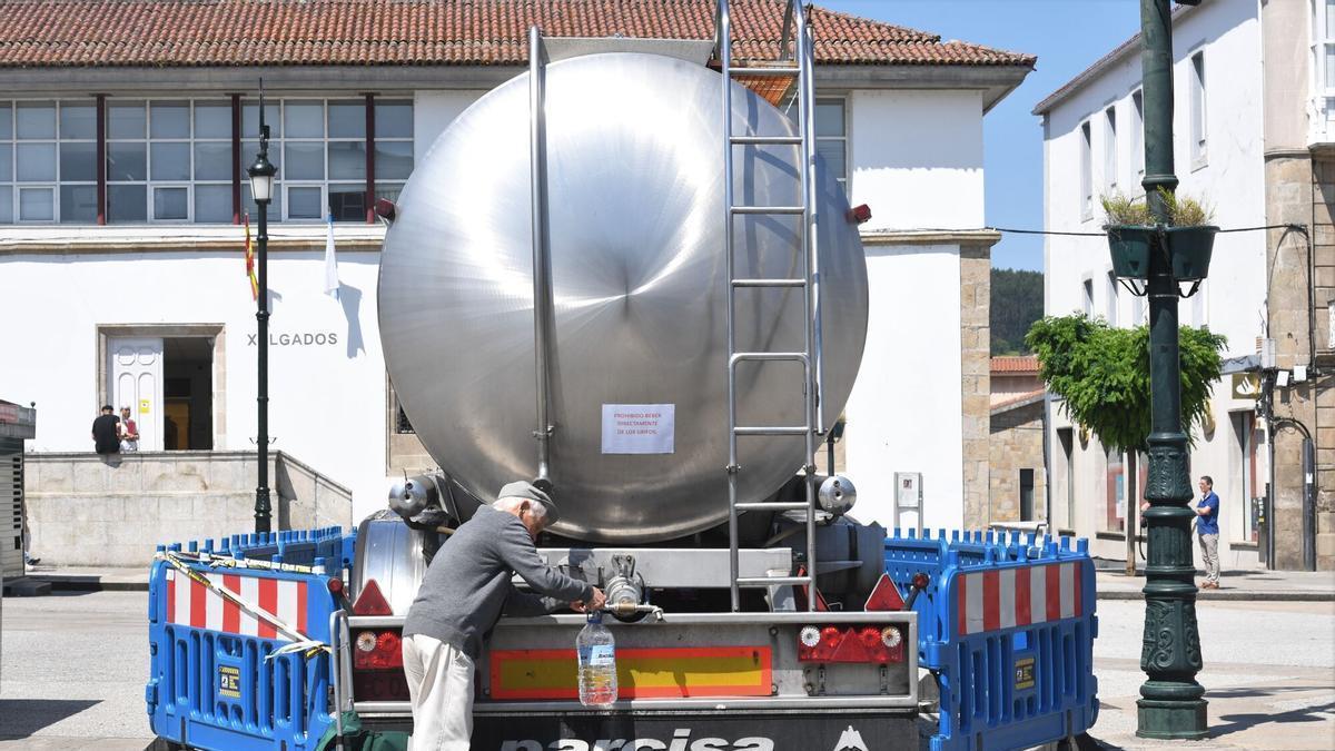 Un hombre se suministra de agua en uno de los camiones cisterta del centro de Betanzos, en verano de 2023