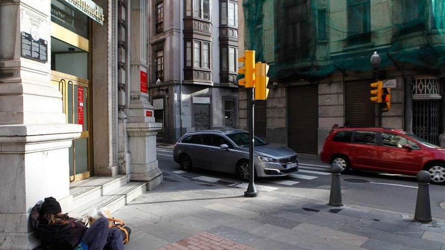 Un mendigo, sentado ante una entidad bancaria del centro de Gijón.