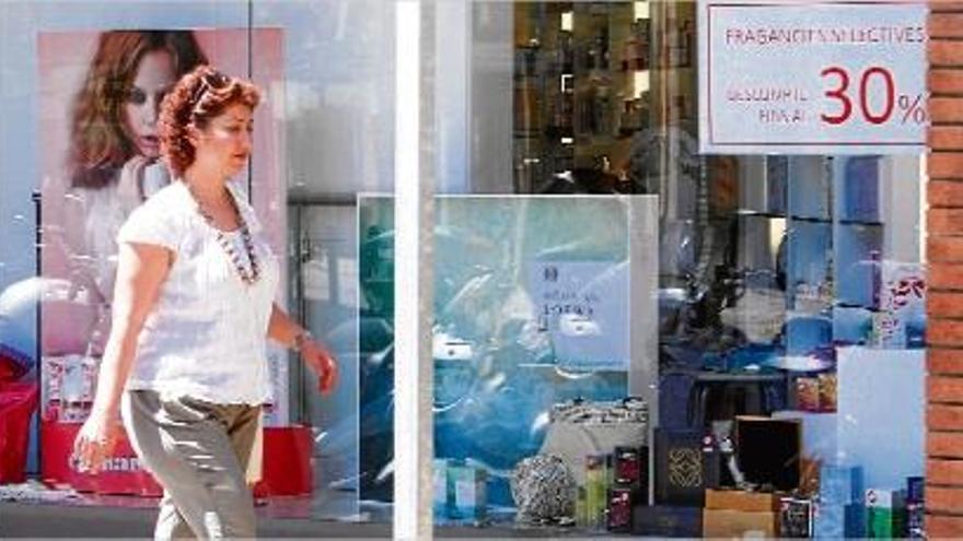 Una dona passa per davant de l&#039;aparador d&#039;una botiga que ofereix productes amb descomptes del 30%.