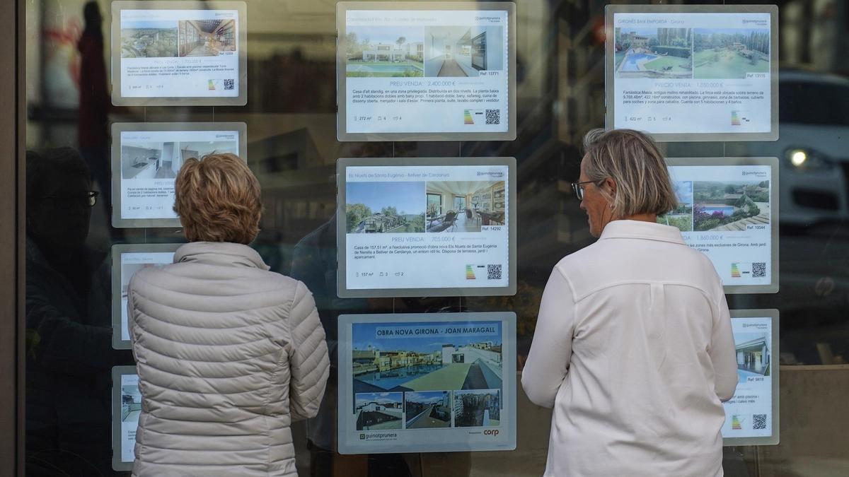 Dues dones davant l’aparador d’una immobiliària a Girona.