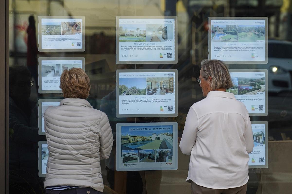 Dues dones davant l’aparador d’una immobiliària a Girona.