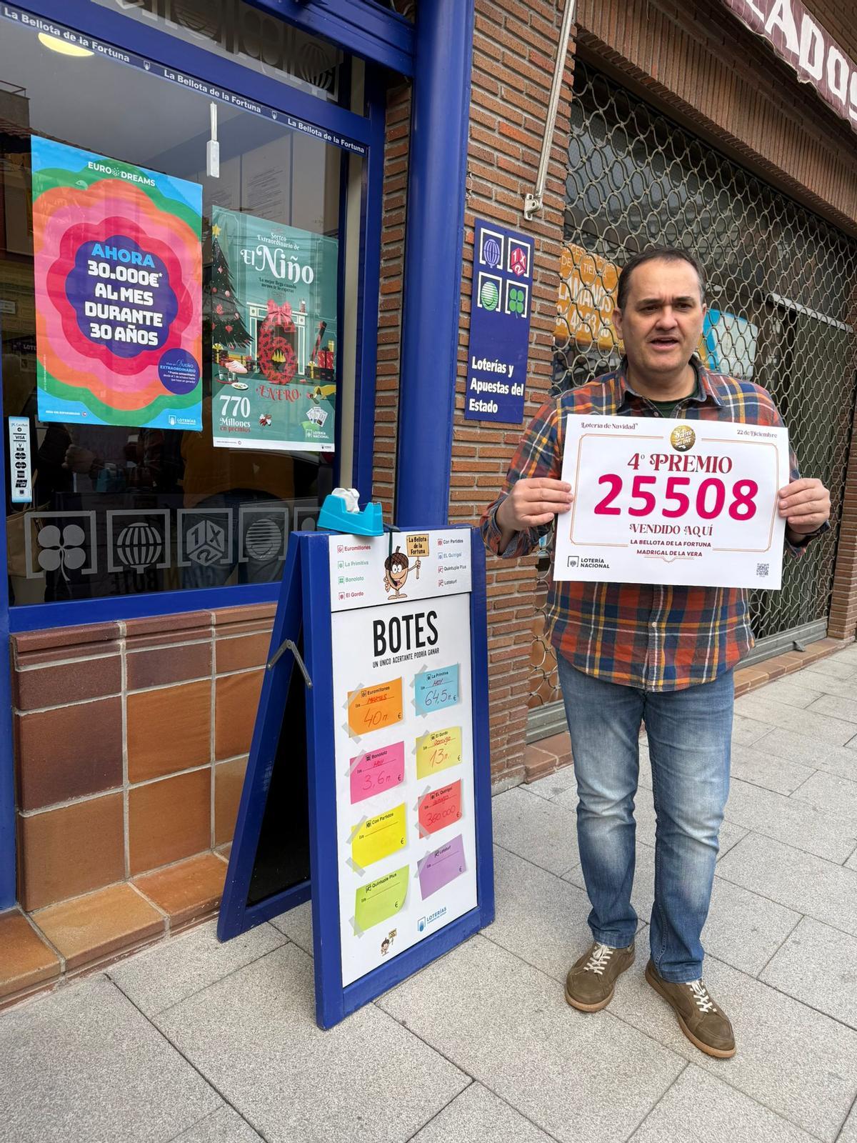 Ángel Luis Carretero, responsable de la administración La Bellota de la Fortuna, en Madrigal de la Vera, muestra el cartel con el número agraciado con un cuarto premio.