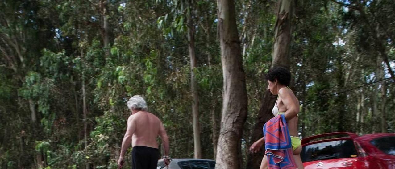 Bañistas pasean por Xagó junto a los coches estacionados.