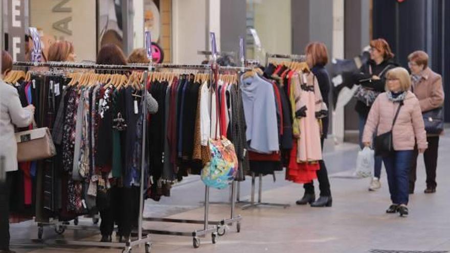 Varias mujeres pasan ante las perchas de una tienda de ropa en la calle Major.