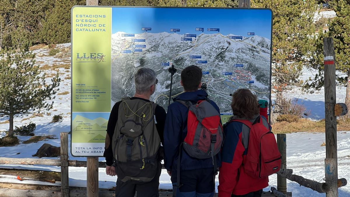 Tres persones observant un itinerari en un cartell situat a la base de l'estació de Lles (Cerdanya)