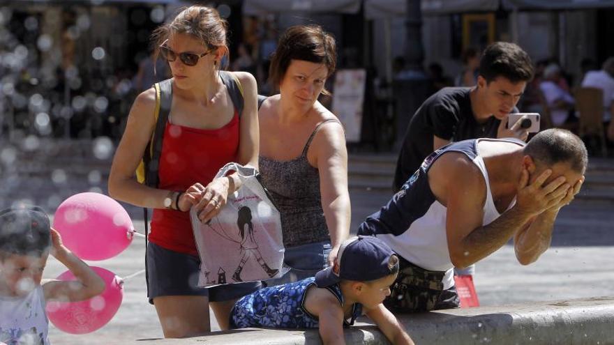 Una familia se refresca en la fuente de la plaza de la Virgen de València, ayer.