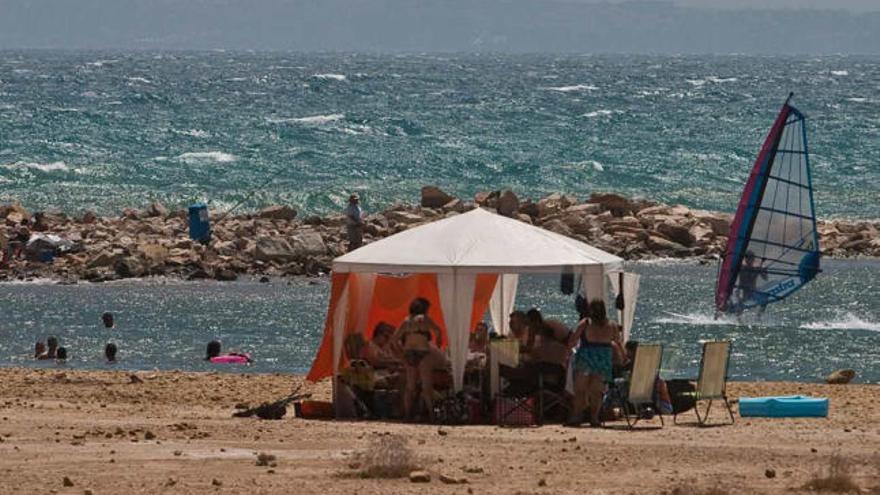 Un joven practica surf a vela cerca de un grupo de bañistas en la zona de Puerto Amor.