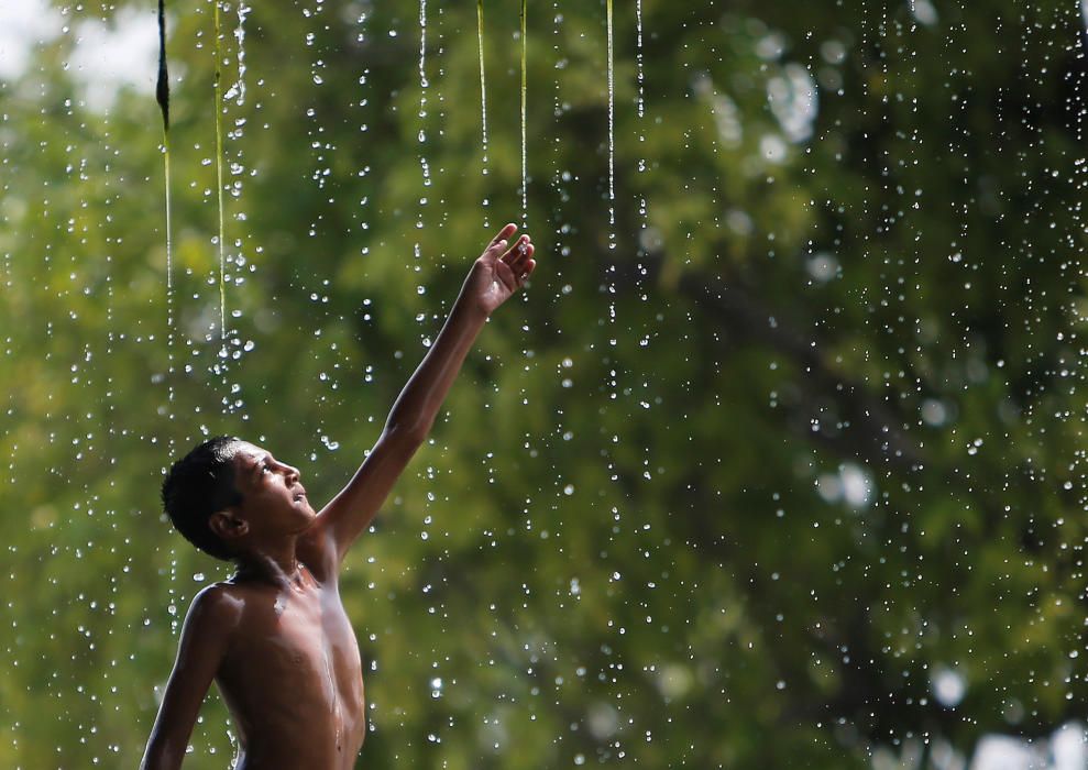 A boy cools off under a water fountain on a hot ...