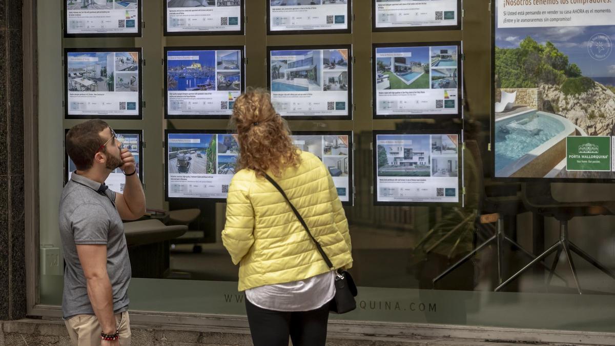 Dos personas miran anuncios de viviendas en una inmobiliaria en Palma.