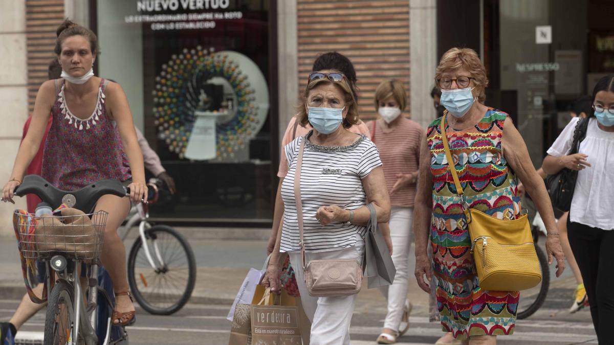 Diverses persones amb la mascareta posada de manera incorrecta passegen pel carrer de Colón, a València.