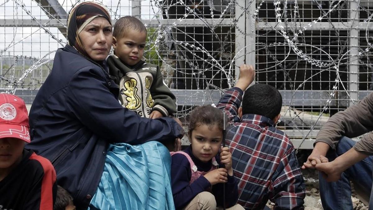 Un mujer migrante rodeada de niños, sentados junto a una valla durante una protesta por las penosas condiciones del campo de refugiados y contra el cierre del paso fronterizo de Idomeni (Grecia), este jueves.