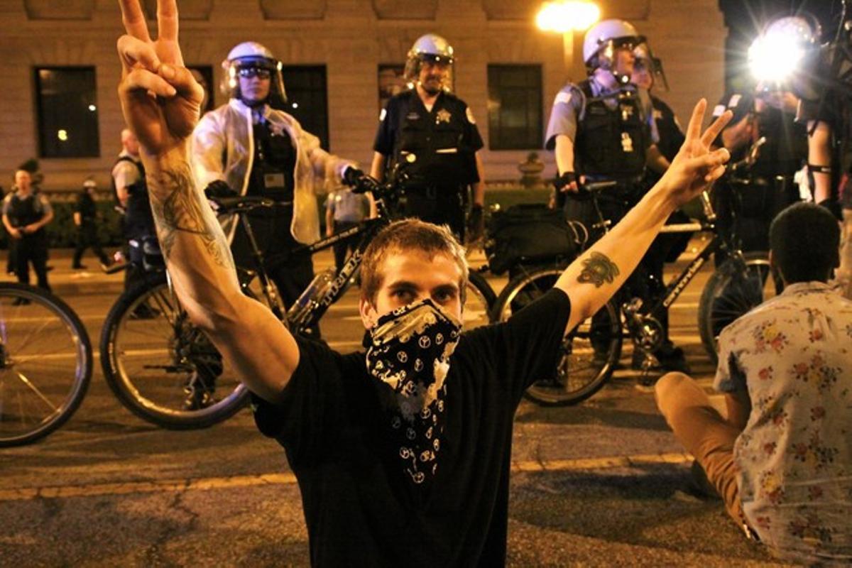 Un encaputxat assegut a terra amb gest de protesta davant la vigilància de la policia de Chicago.