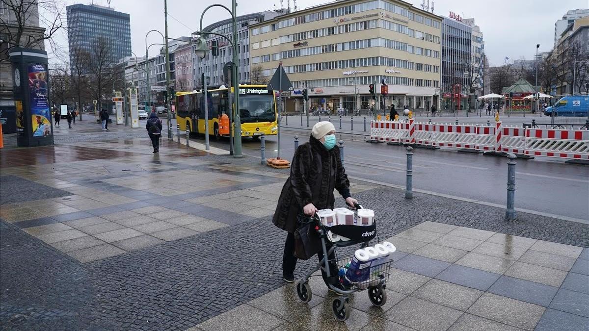 Una anciana con una máscara protectora empuja un carrito cargado de papel higiénico y toallas de papel, este lunes, en Berlín.