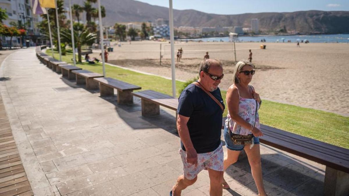 Dos turistas transitan por el paseo de la playa de Los Cristianos, en el municipio de Arona.