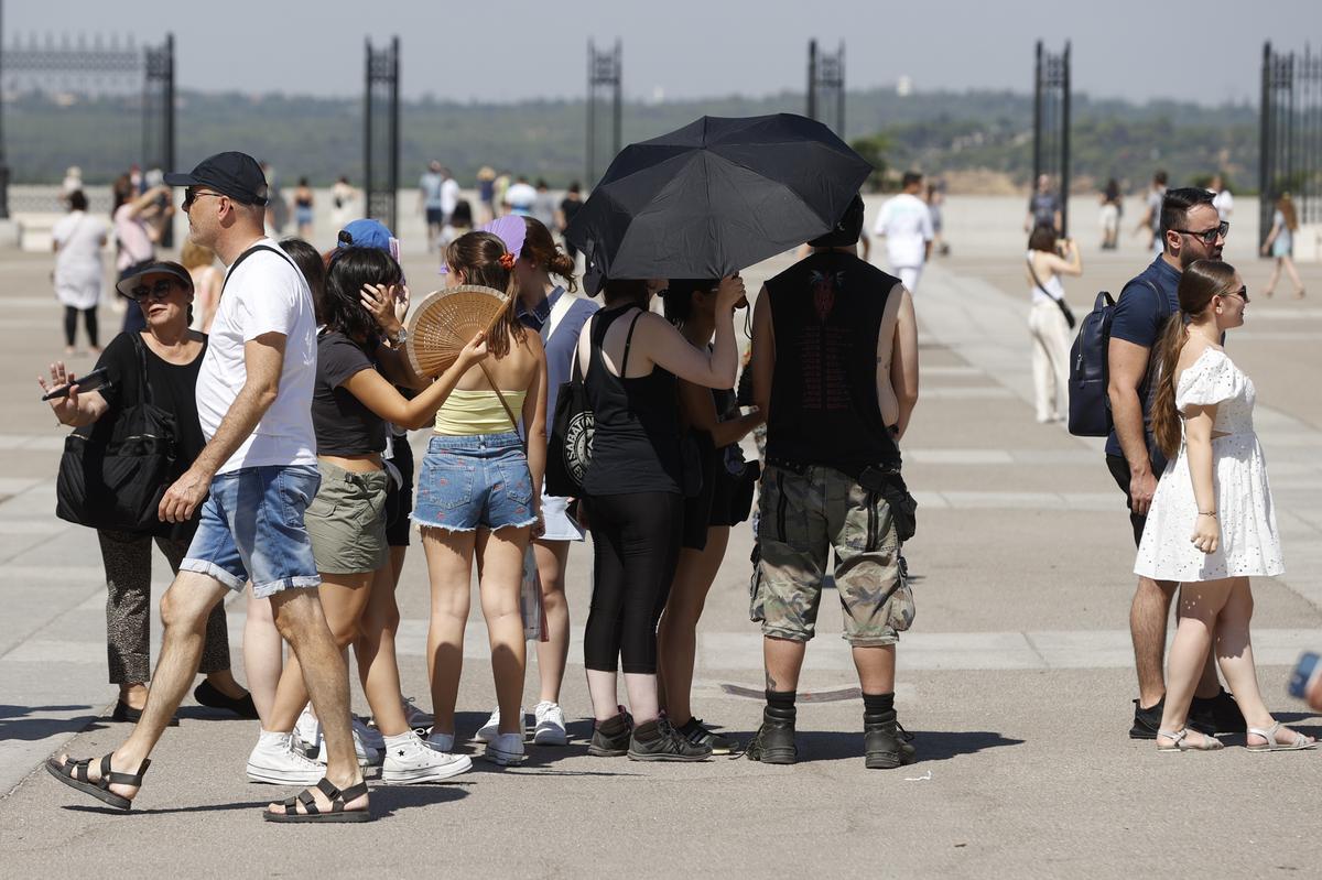 Varios turistas pasean por la calle ataviados con gorras, paraguas y abanicos para protegerse del sol.