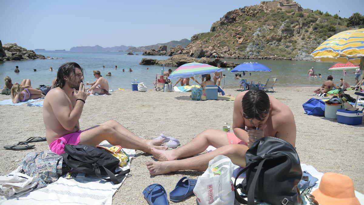 Dos jóvenes fuman sus cigarrillos en la playa de La Cortina, en Cartagena.