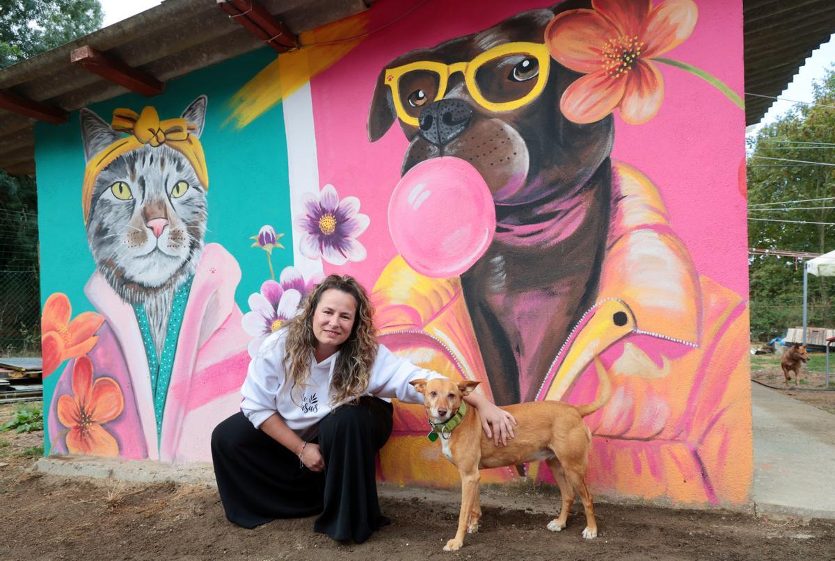 Eva Casais, ayer, con la perrita Rosca ante el mural que pintó recientemente en la protectora Os Biosbardos