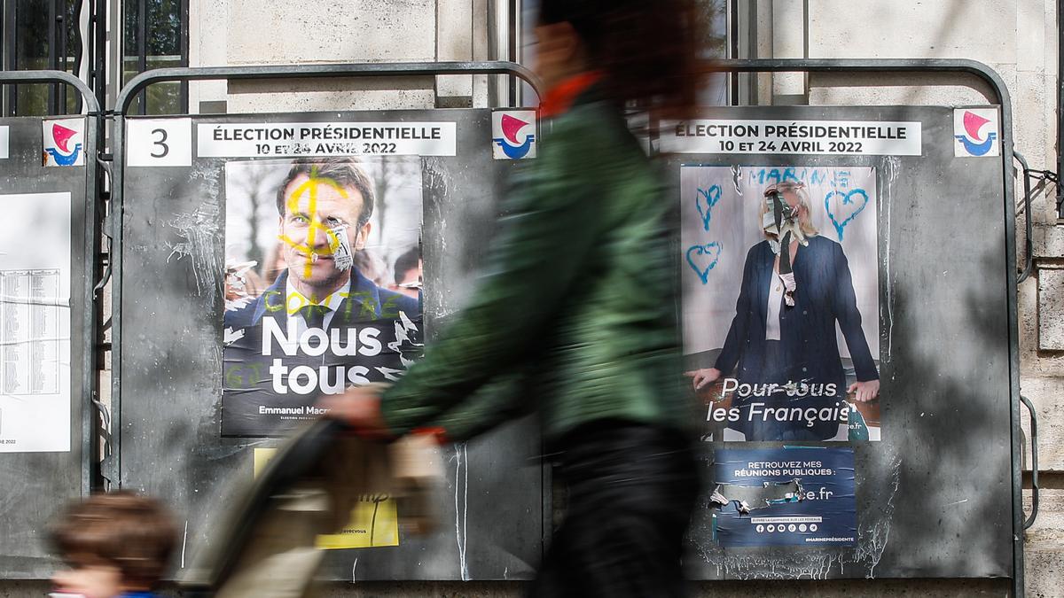 Una mujer pasa frente a los carteles electorales de Macron y Le Pen en una calle de París.