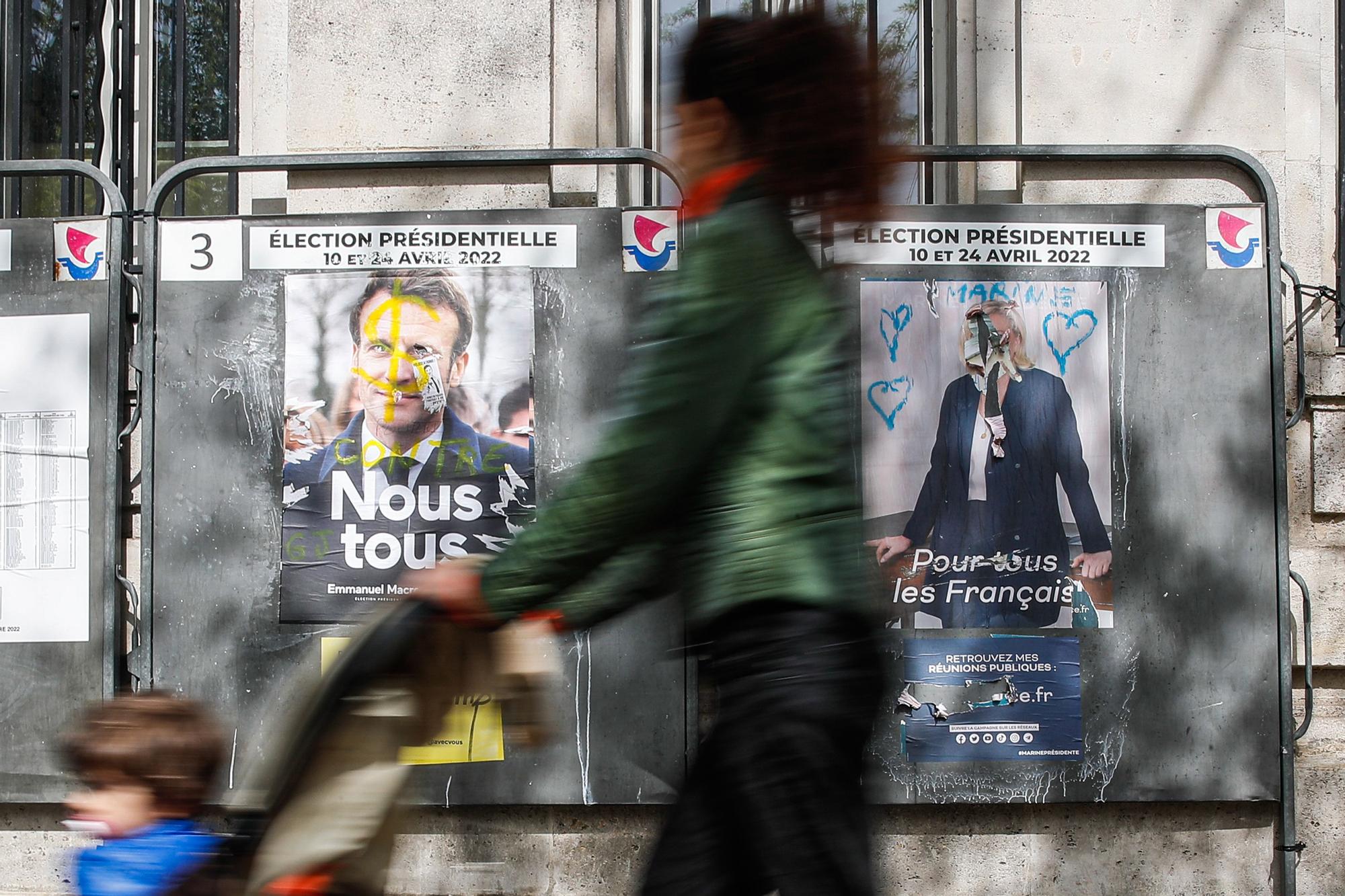 Una mujer pasa frente a los carteles electorales de Macron y Le Pen en una calle de París.