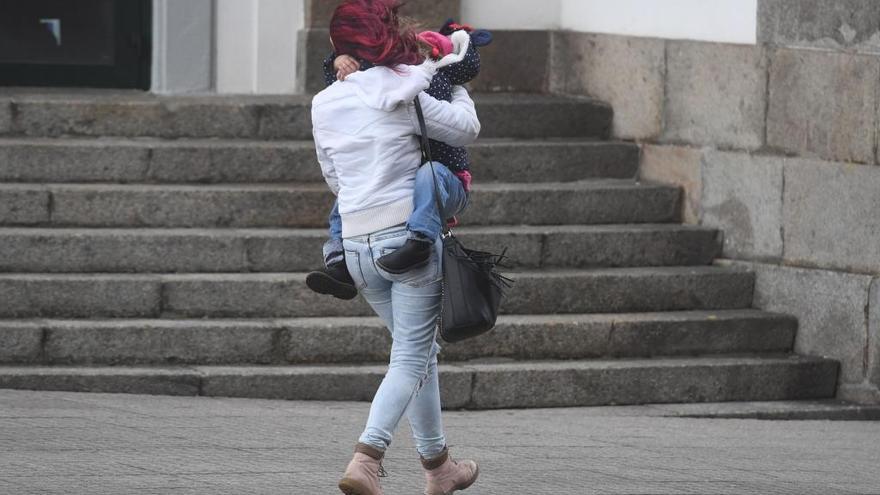 Una mujer con un menor en brazos sortea el viento en A Coruña.
