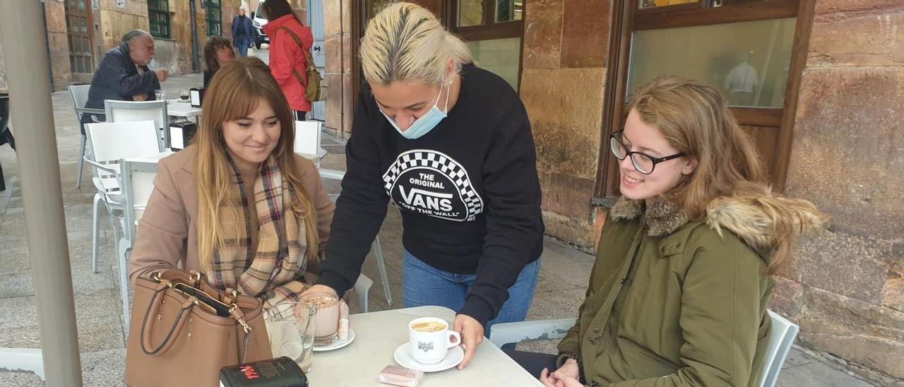 Liliana Fernández, en el centro, sirve unos cafés a Helena Suárez y Sandra Muñiz en una terraza de la plaza del Sol. | L. B.