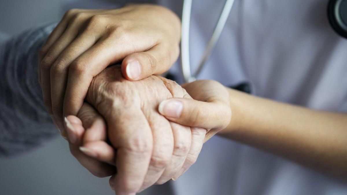 Una sanitaria sujeta las manos de una mujer anciana