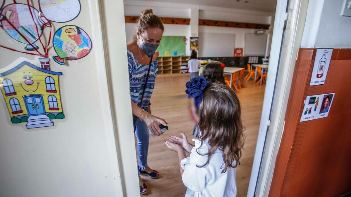 Una maestra pone gel hidroalcohólico a una niña antes de entrar en clase