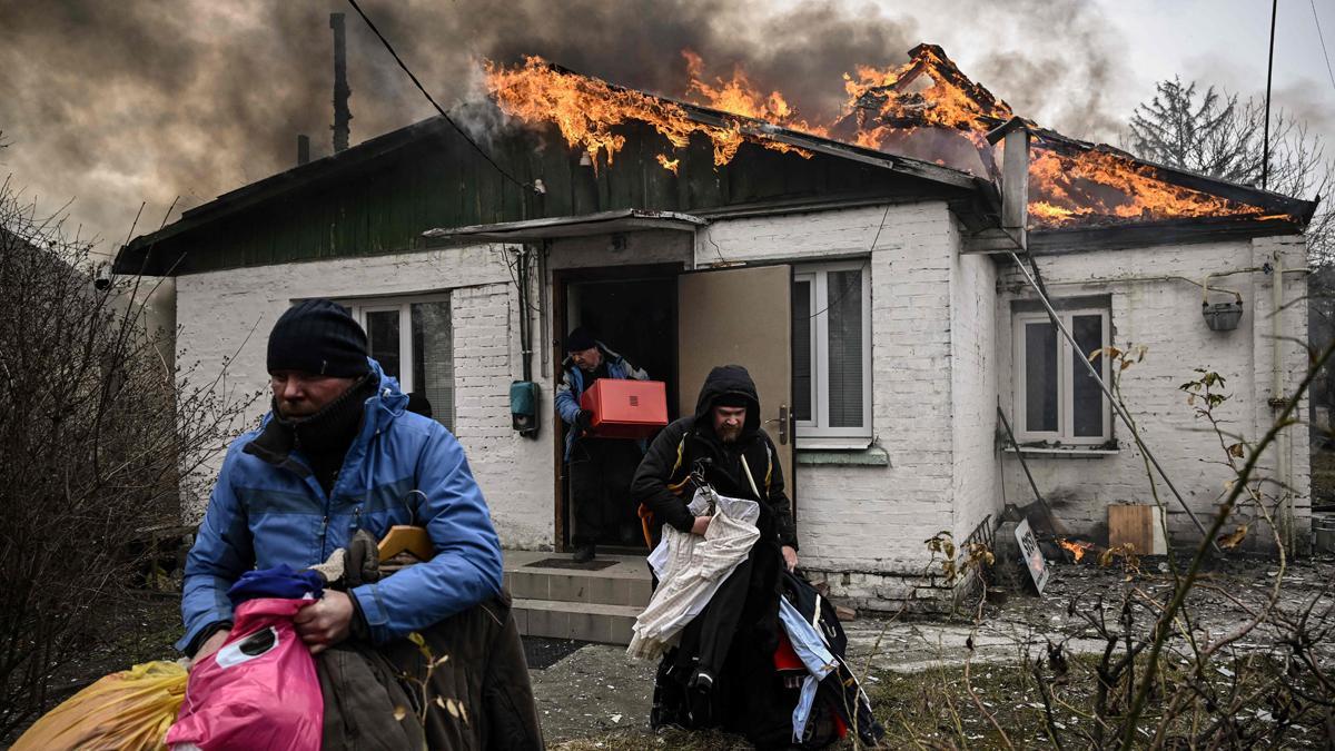 La gente saca sus pertenencias personales de una casa en llamas después de ser bombardeada en la ciudad de Irpin, en las afueras de Kiev